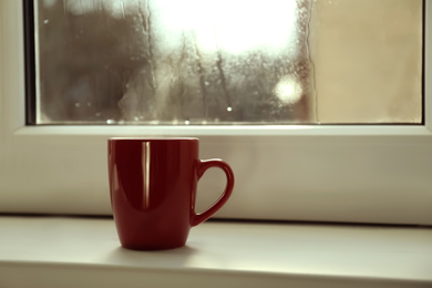 Cup of hot drink near window on rainy day. Space for text