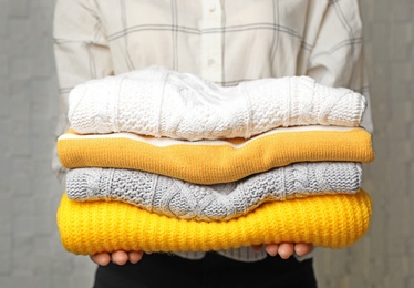 Photo of Woman holding stack of folded warm knitted sweaters, closeup