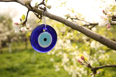 Photo of Evil eye amulet hanging on blossoming spring tree outdoors, closeup