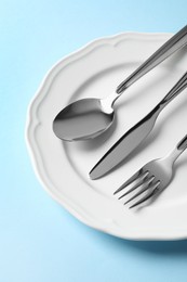 Photo of Stylish silver cutlery and plate on light blue background, above view