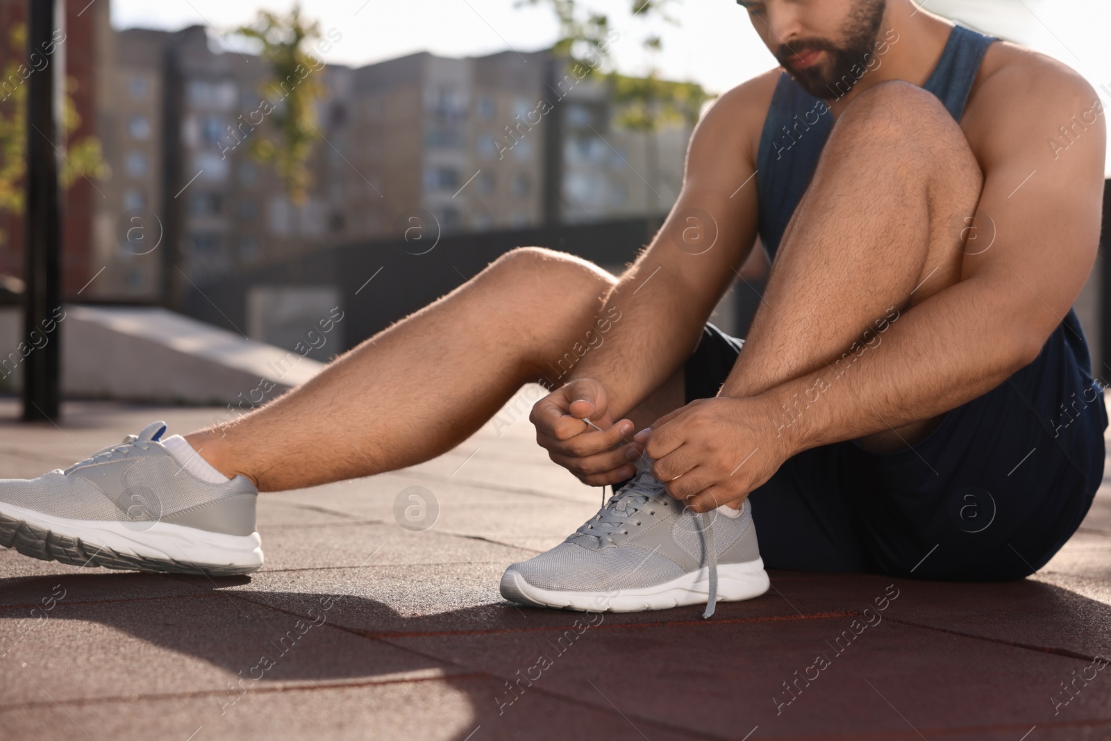 Photo of Man tying shoelaces before running outdoors on sunny day, closeup