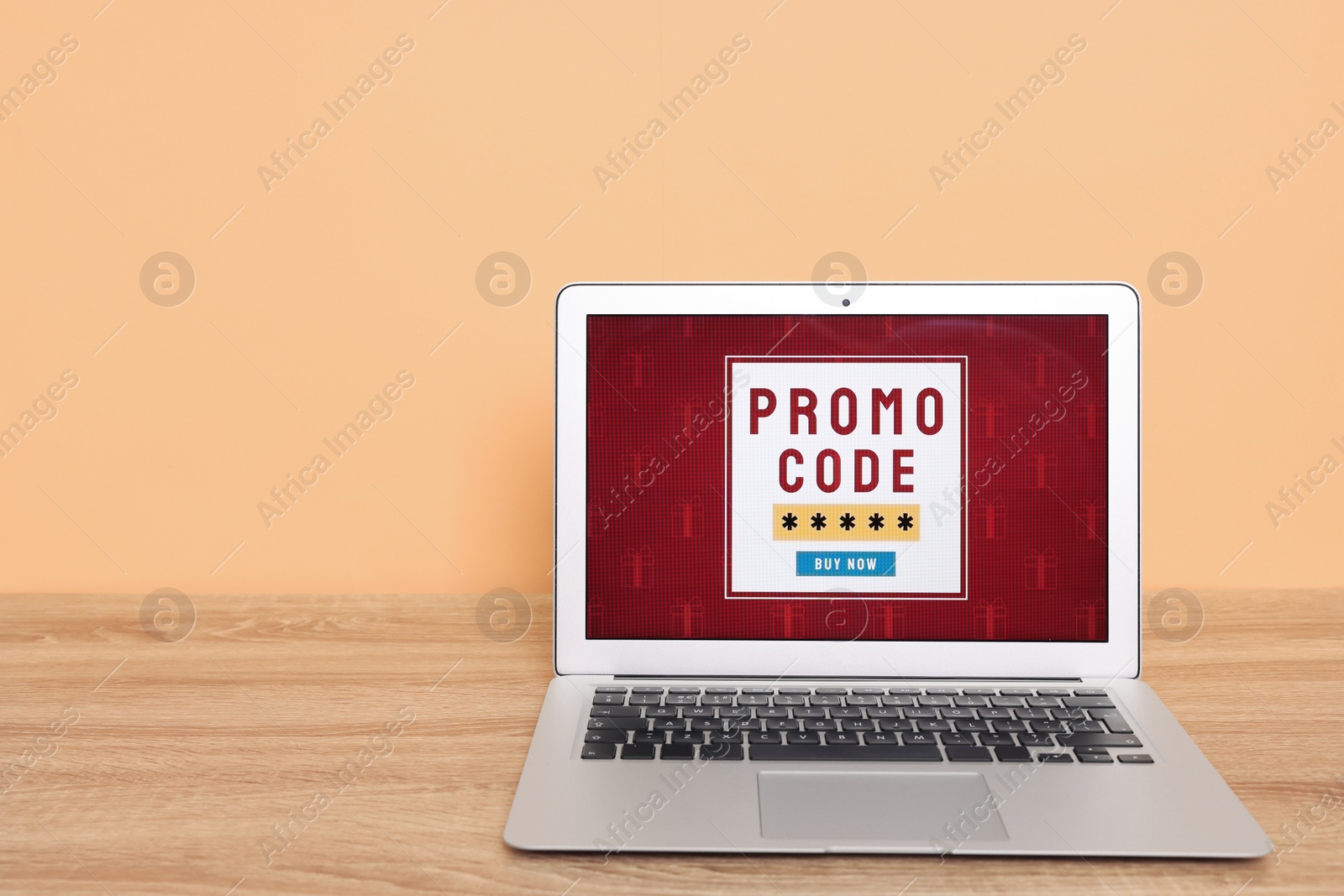 Photo of Laptop with activated promo code on wooden table near beige wall. Space for text