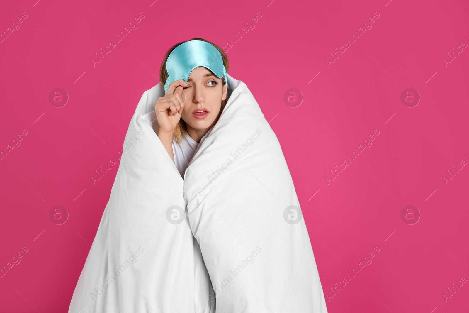 Photo of Young woman in sleeping mask wrapped with soft blanket on pink background. Space for text