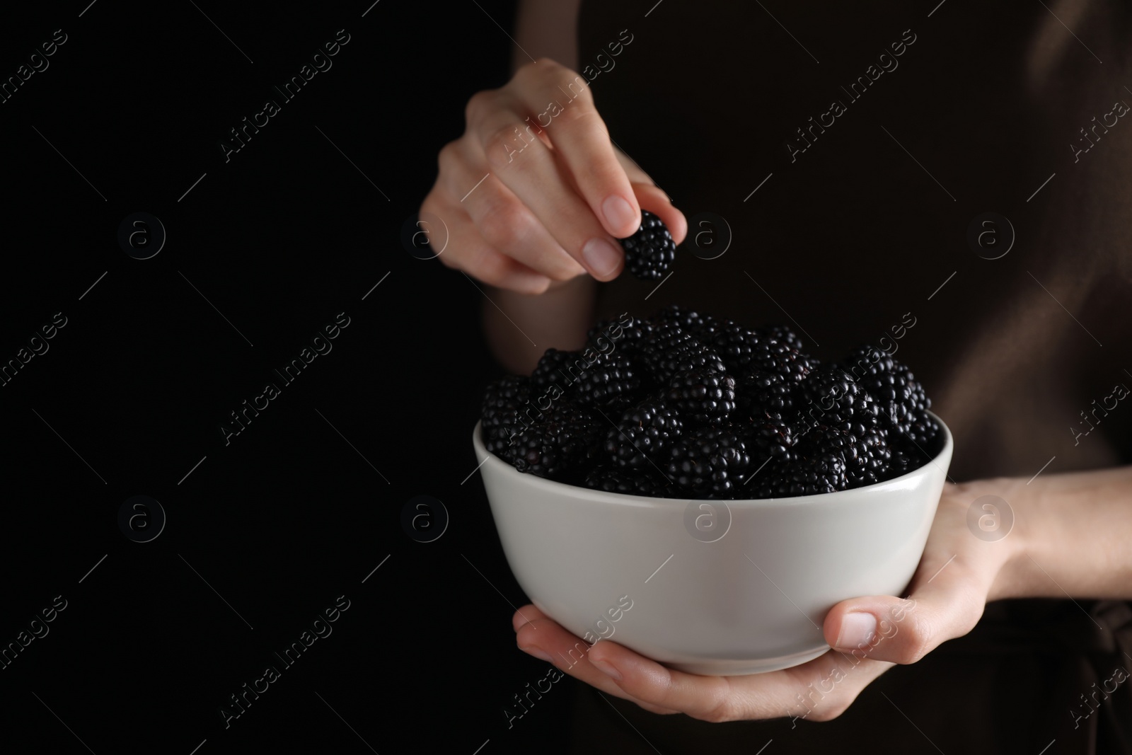 Photo of Woman with bowl of fresh blackberries against dark background, closeup