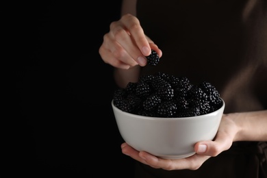 Photo of Woman with bowl of fresh blackberries against dark background, closeup