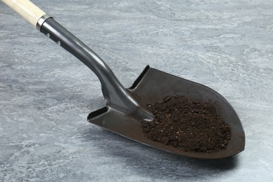 Photo of Metal shovel with fertile soil on gray textured surface