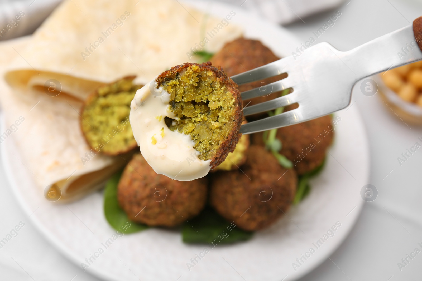 Photo of Eating delicious falafel ball with sauce at table, closeup