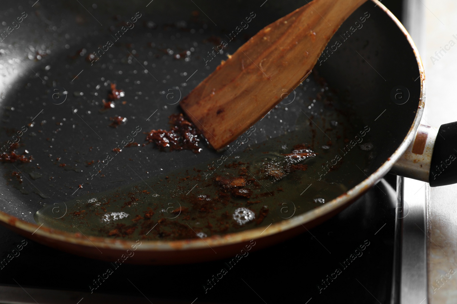 Photo of Frying pan with spatula and used cooking oil on stove, closeup