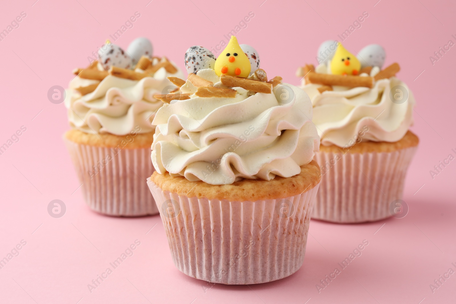 Photo of Tasty Easter cupcakes with vanilla cream on pink background, closeup