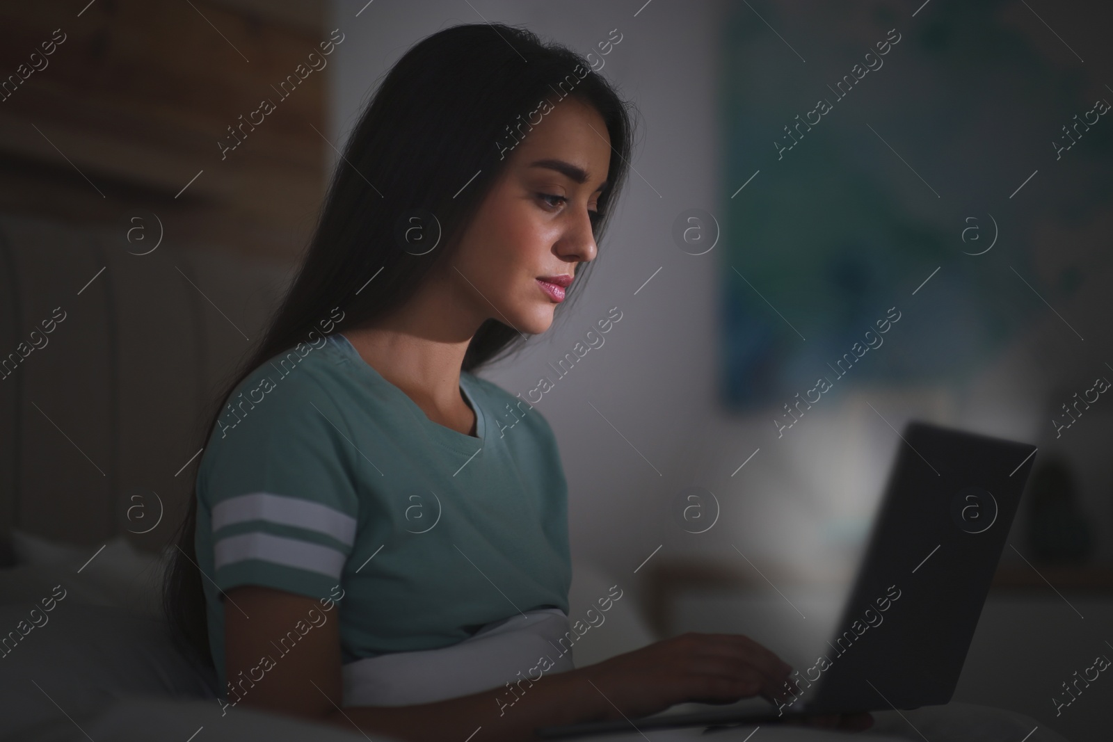 Photo of Young woman with nomophobia using laptop in bed at night. Insomnia concept