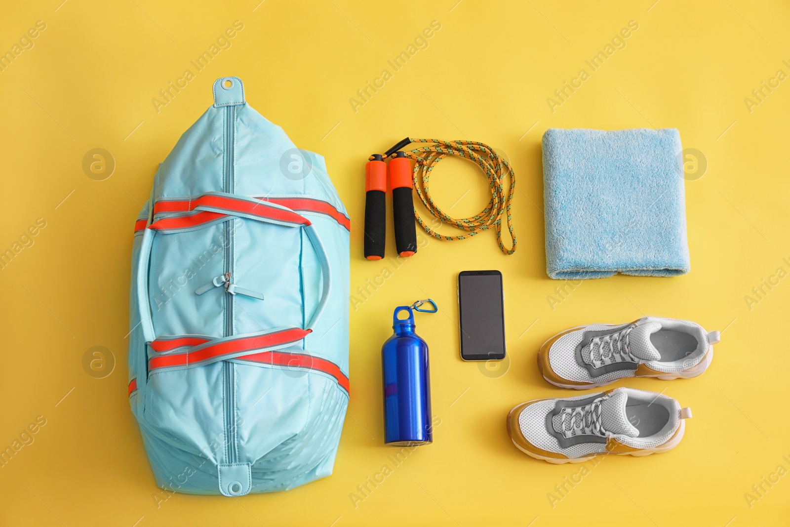 Photo of Gym bag, smartphone and sports equipment on yellow background, flat lay