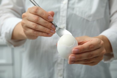 Photo of Woman eating boiled egg with spoon on blurred background, closeup