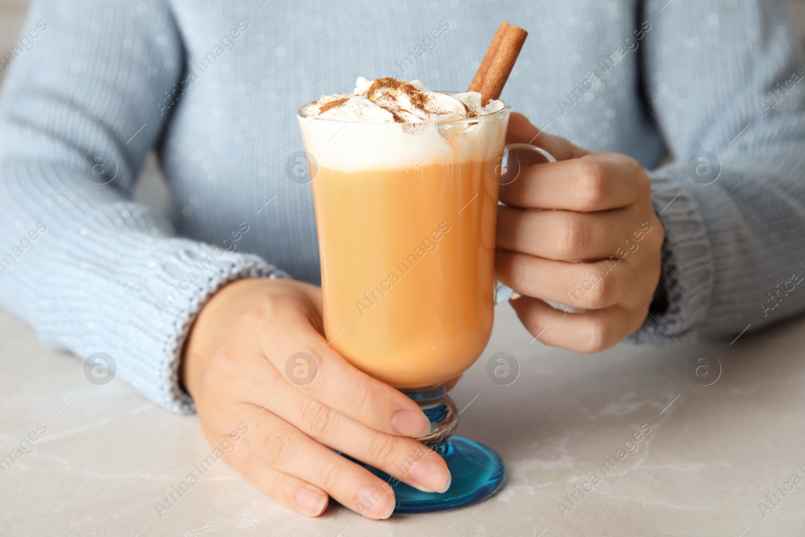 Photo of Woman holding glass cup with pumpkin spice latte and whipped cream on light table