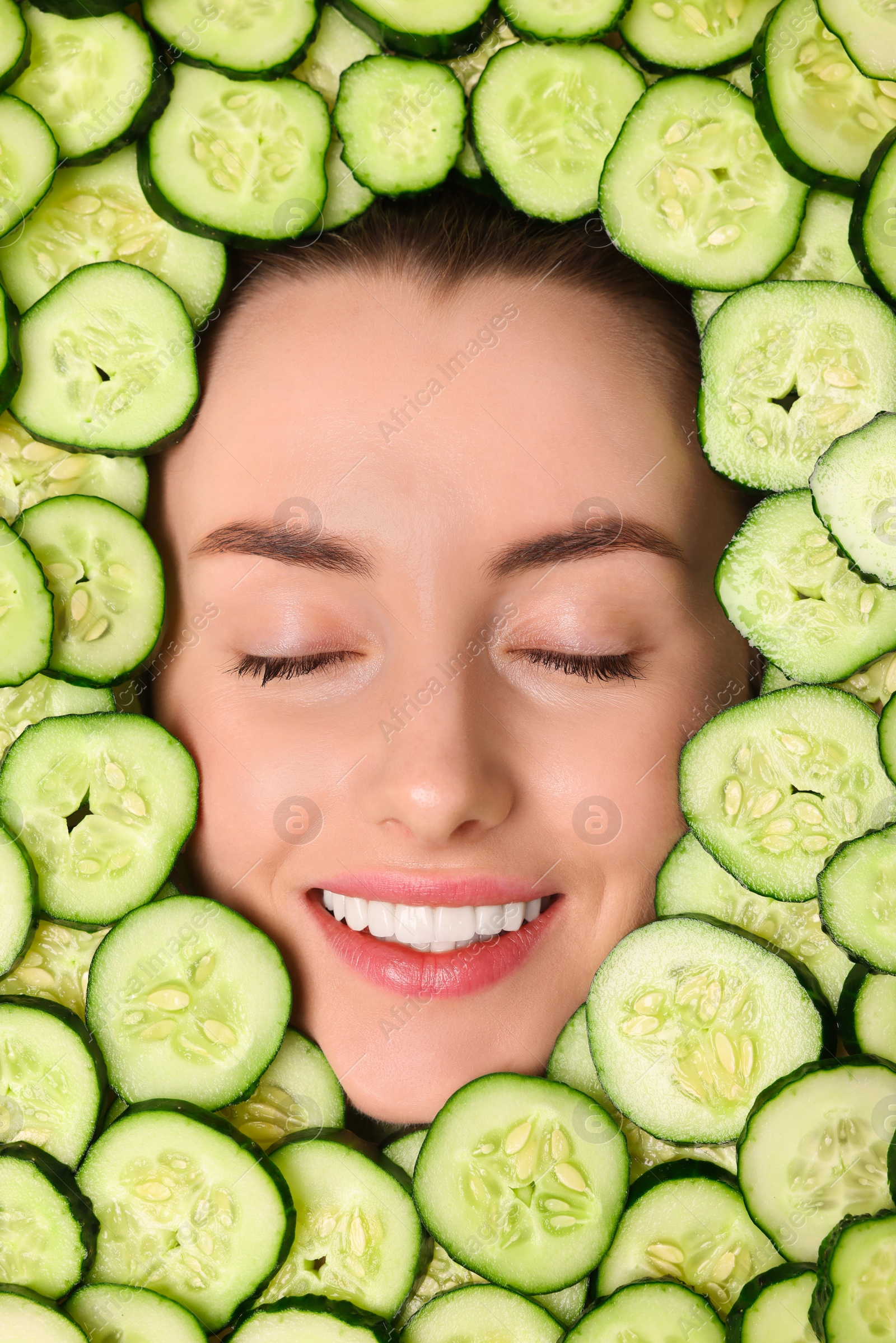 Photo of Beautiful woman among cucumber slices, top view