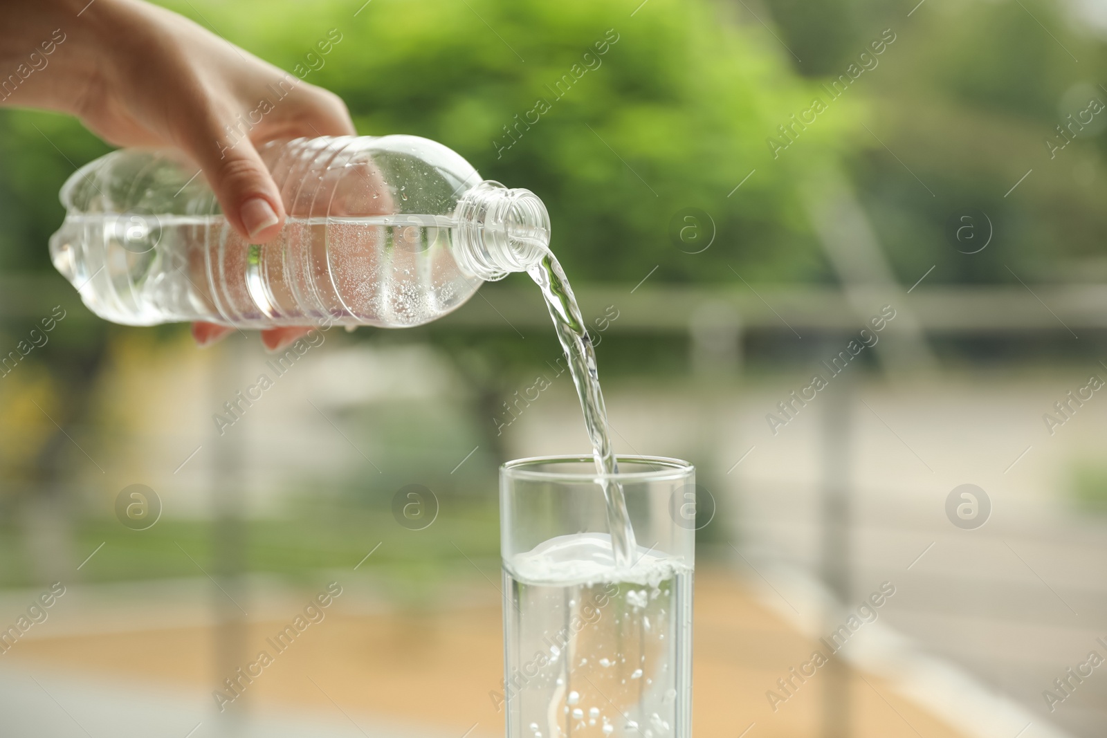 Photo of Woman pouring water from bottle into glass against blurred background, closeup