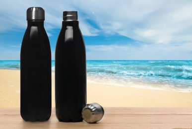 Thermo bottles on wooden table near sea under blue sky