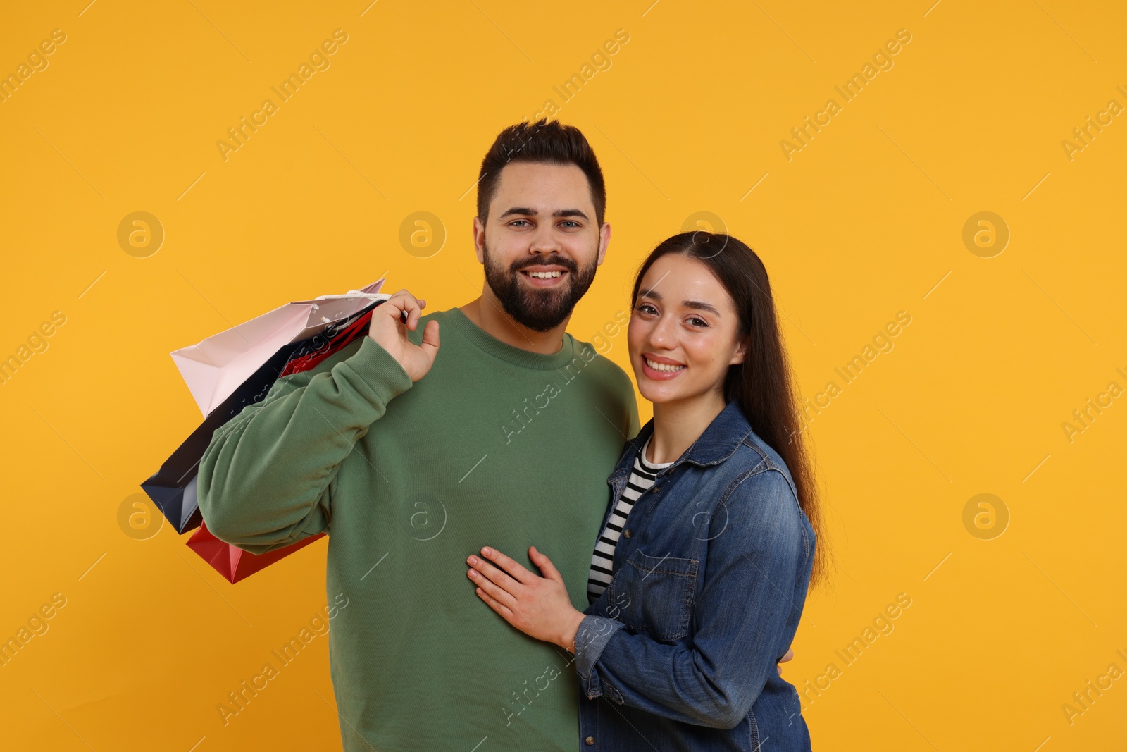 Photo of Happy couple with shopping bags on orange background