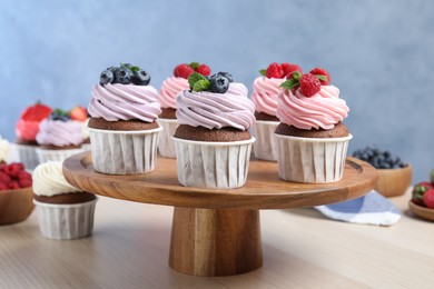 Photo of Wooden dessert stand with sweet cupcakes on light table