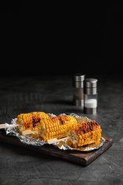 Delicious grilled corn cobs on table against black background. Space for text