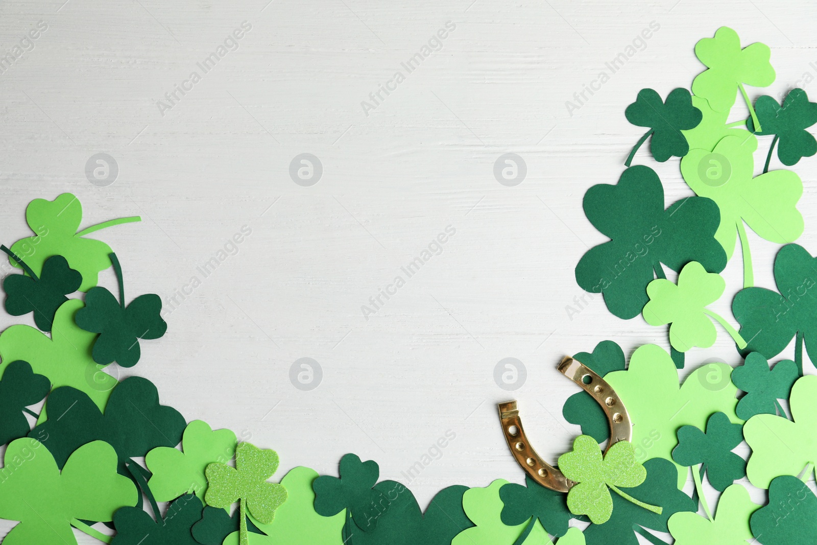 Photo of Flat lay composition with clover leaves and horseshoe on white wooden background, space for text. St. Patrick's day