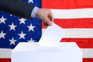 Image of Election in USA. Man putting his vote into ballot box and American flag on background, closeup
