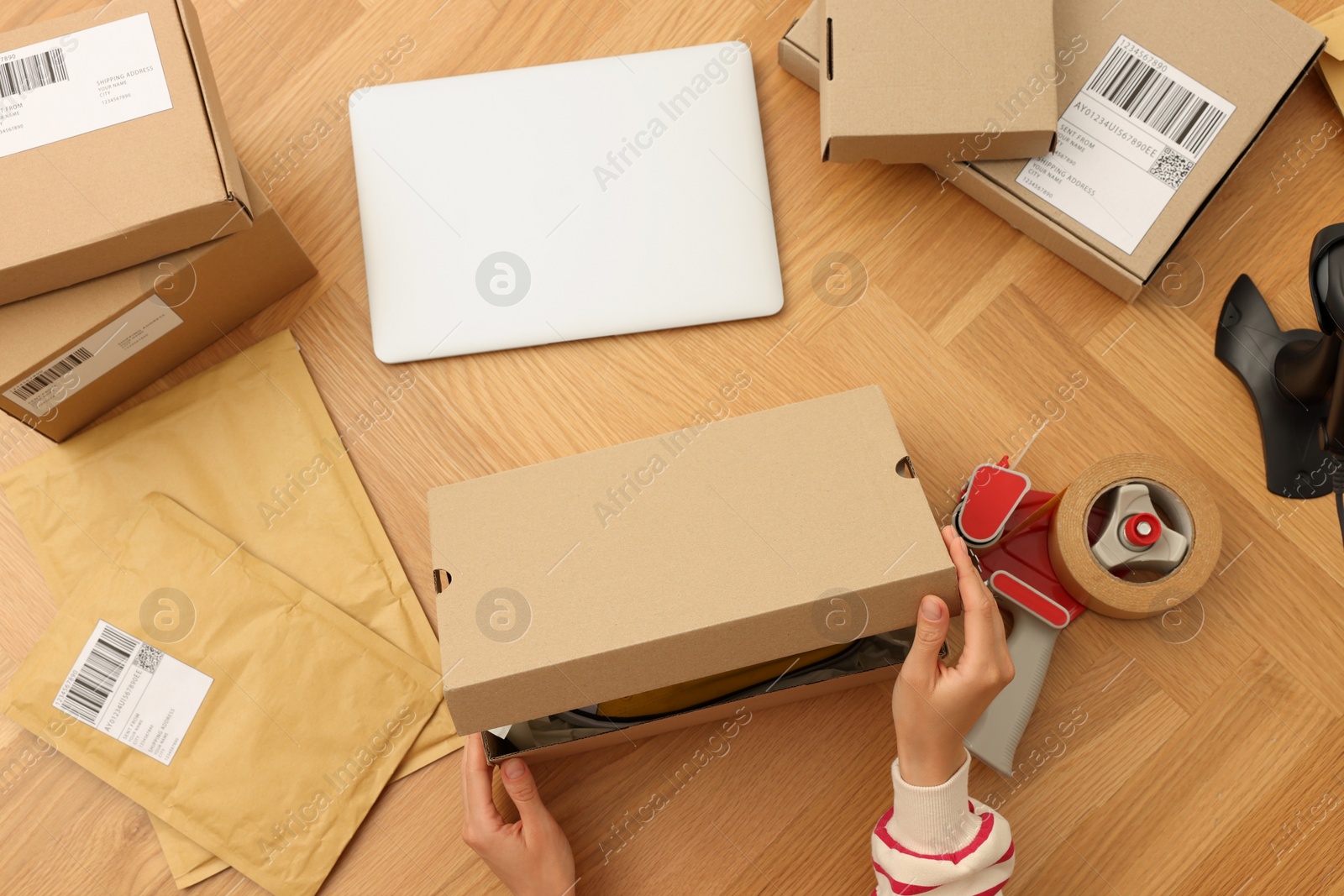 Photo of Woman packing cardboard box at wooden table, top view. Online store