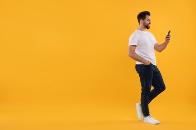 Happy young man using smartphone on yellow background, space for text