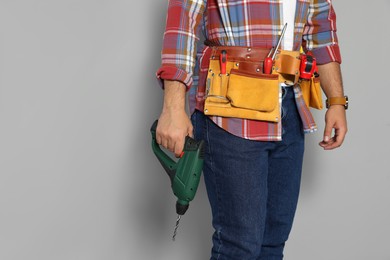 Photo of Worker with power drill and tool belt on grey background, closeup. Space for text