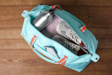 Photo of Open sports bag full of gym stuff on wooden background, top view