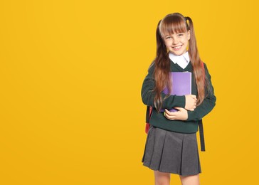 Little girl in stylish school uniform on yellow background, space for text