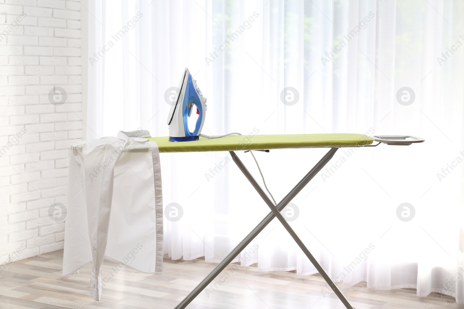 Photo of Board with modern iron and shirt at home. Laundry day