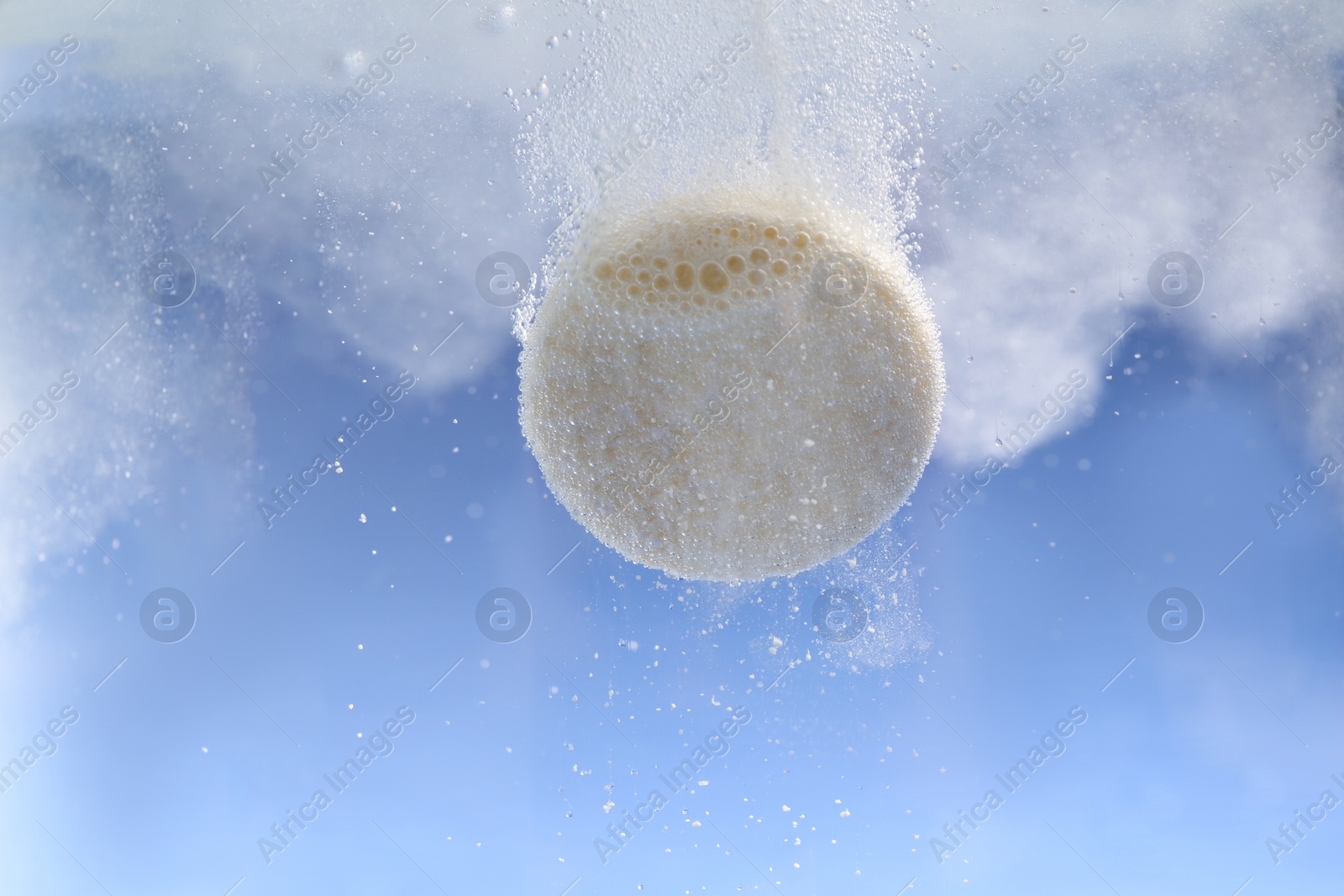 Photo of Effervescent pill dissolving in water on light blue background, closeup