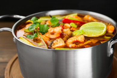 Photo of Saucepan with delicious Tom Yum soup on wooden board, closeup