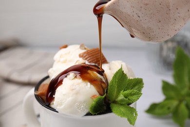 Pouring caramel sauce onto ice cream with candies and mint leaves, closeup