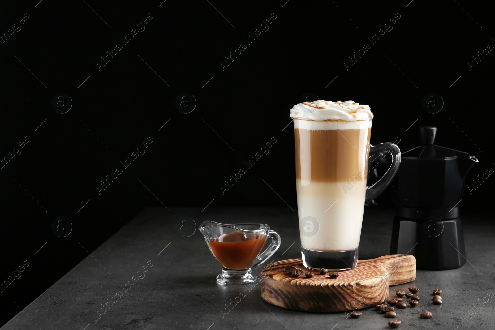 Photo of Glass cup of caramel macchiato and gravy boat with syrup on table, space for text