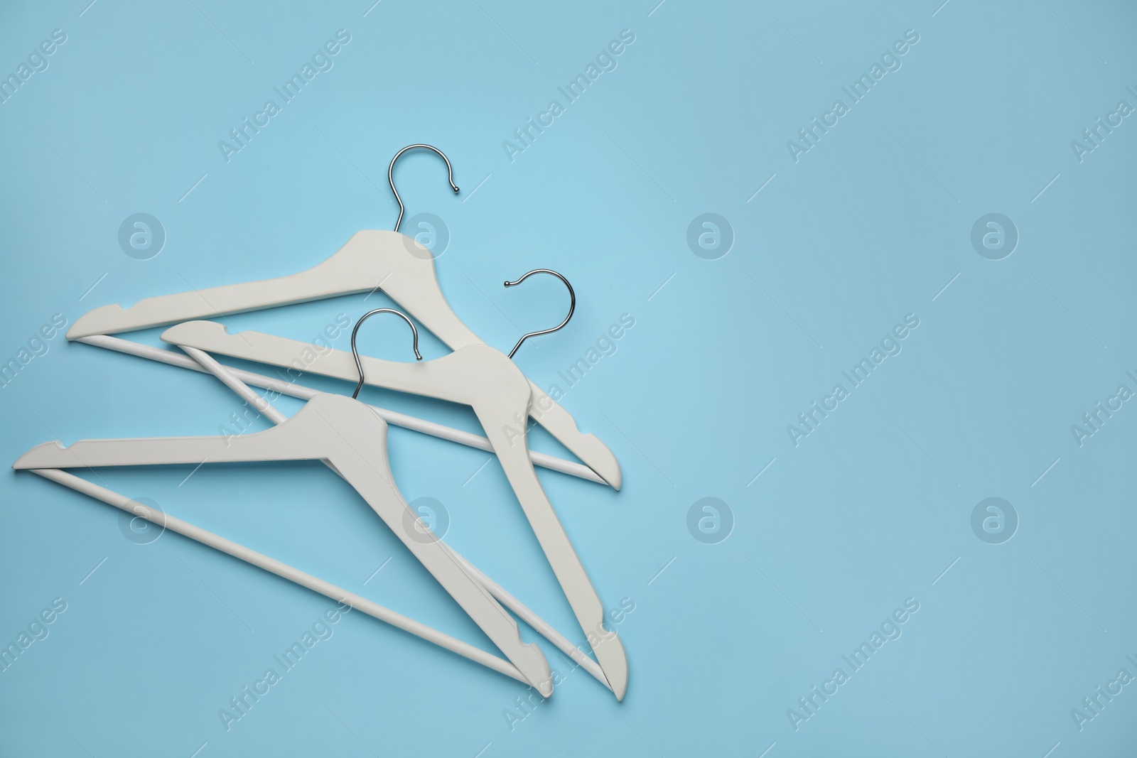 Photo of Empty clothes hangers on light blue background, flat lay. Space for text