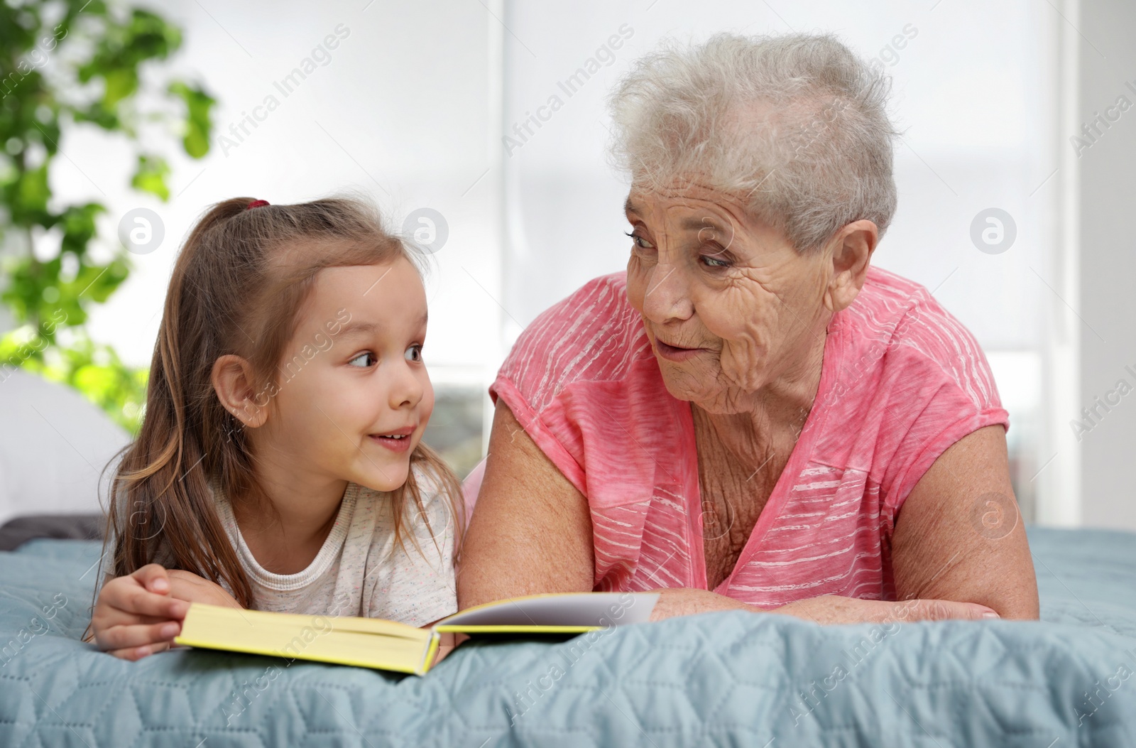 Photo of Cute girl and her grandmother reading book on bed at home