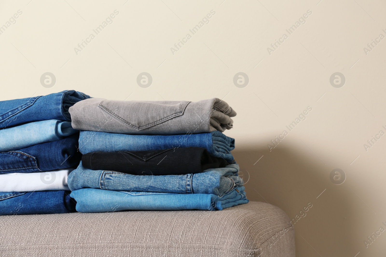 Photo of Stack of different jeans on ottoman against light background