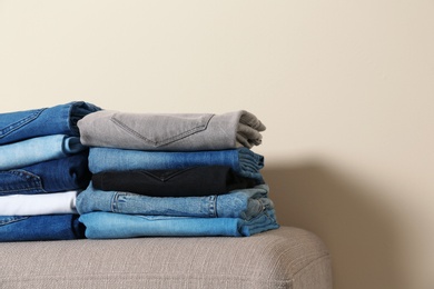 Photo of Stack of different jeans on ottoman against light background