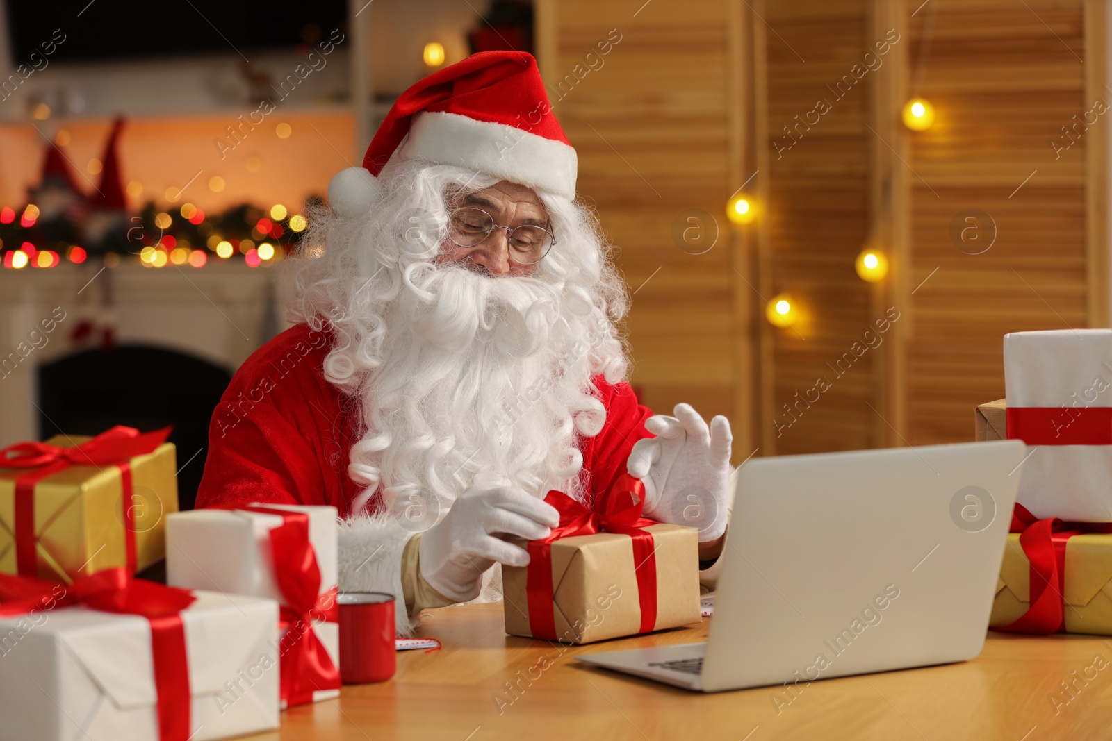Photo of Santa Claus decorating Christmas gift with ribbon at home