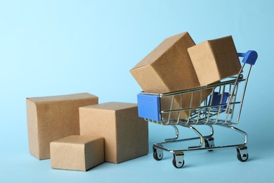 Photo of Shopping cart and boxes on light blue background. Logistics and wholesale concept