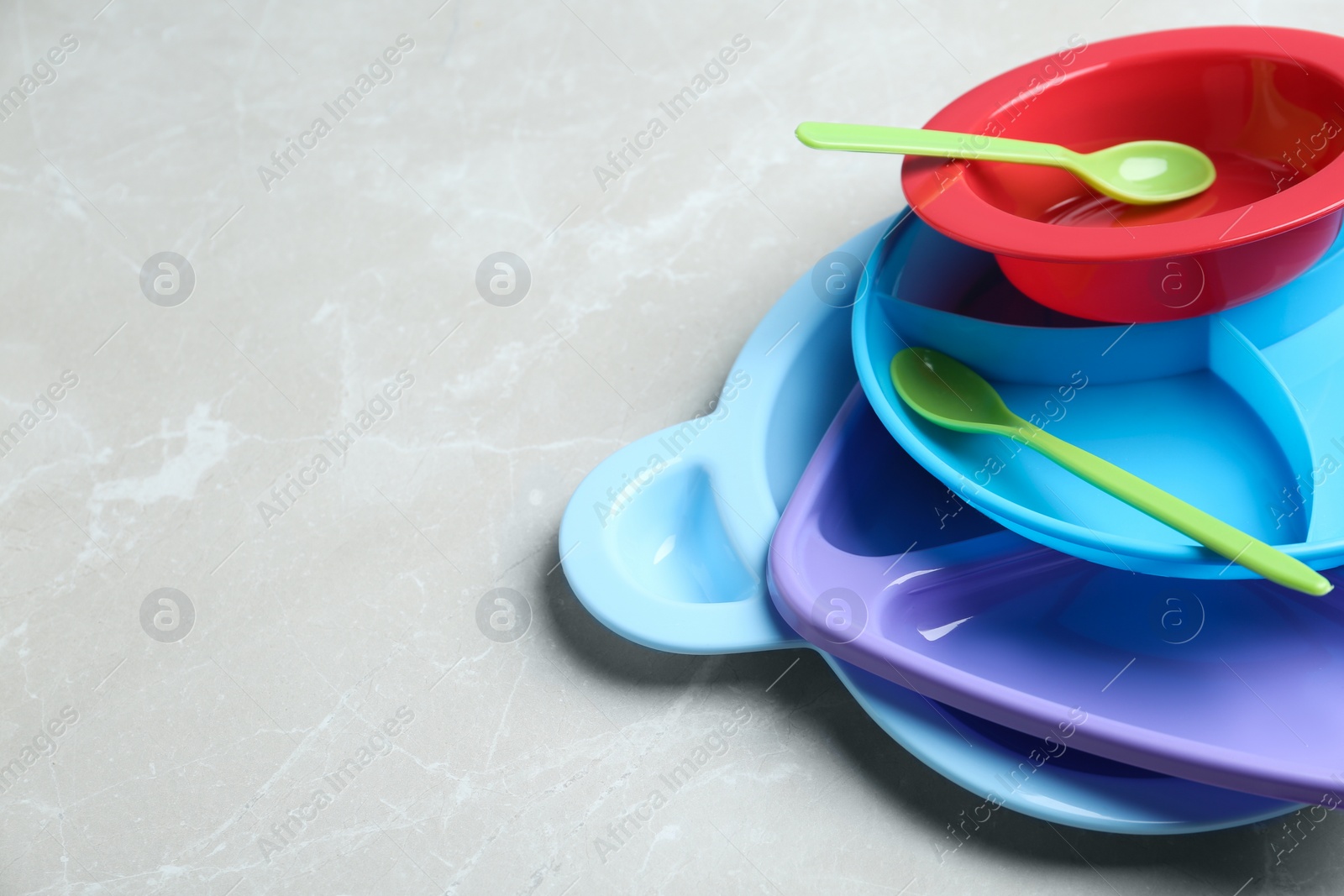 Photo of Pile of colorful plastic dishware on light grey marble table, space for text. Serving baby food