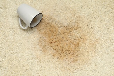 Photo of Overturned cup and spilled drink on beige carpet, top view