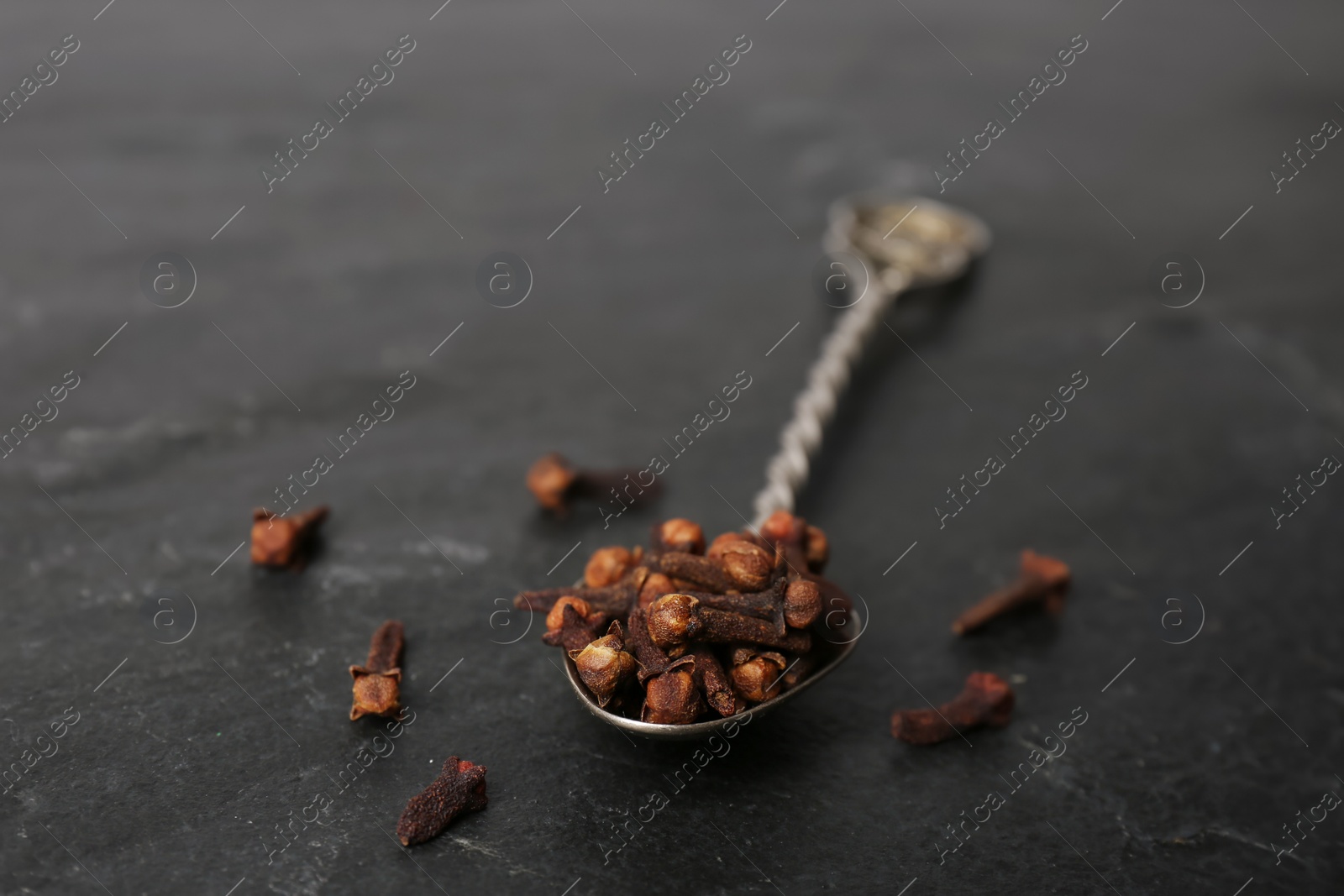 Photo of Aromatic dry cloves with spoon on black table