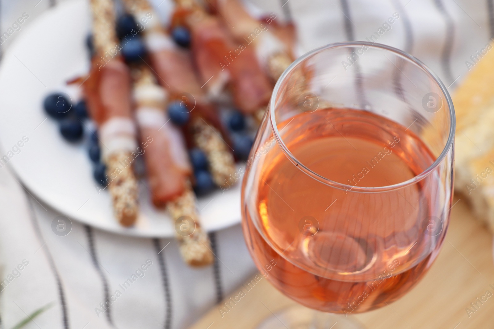 Photo of Glass of delicious rose wine and food on white picnic blanket, closeup