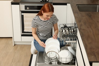 Smiling woman loading dishwasher with plates in kitchen