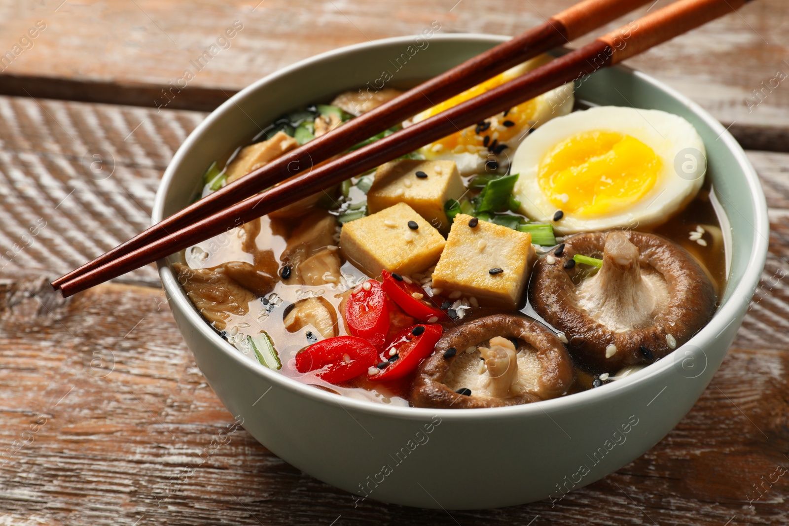 Photo of Bowl of delicious ramen and chopsticks on wooden table, closeup. Noodle soup