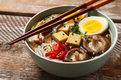 Bowl of delicious ramen and chopsticks on wooden table, closeup. Noodle soup