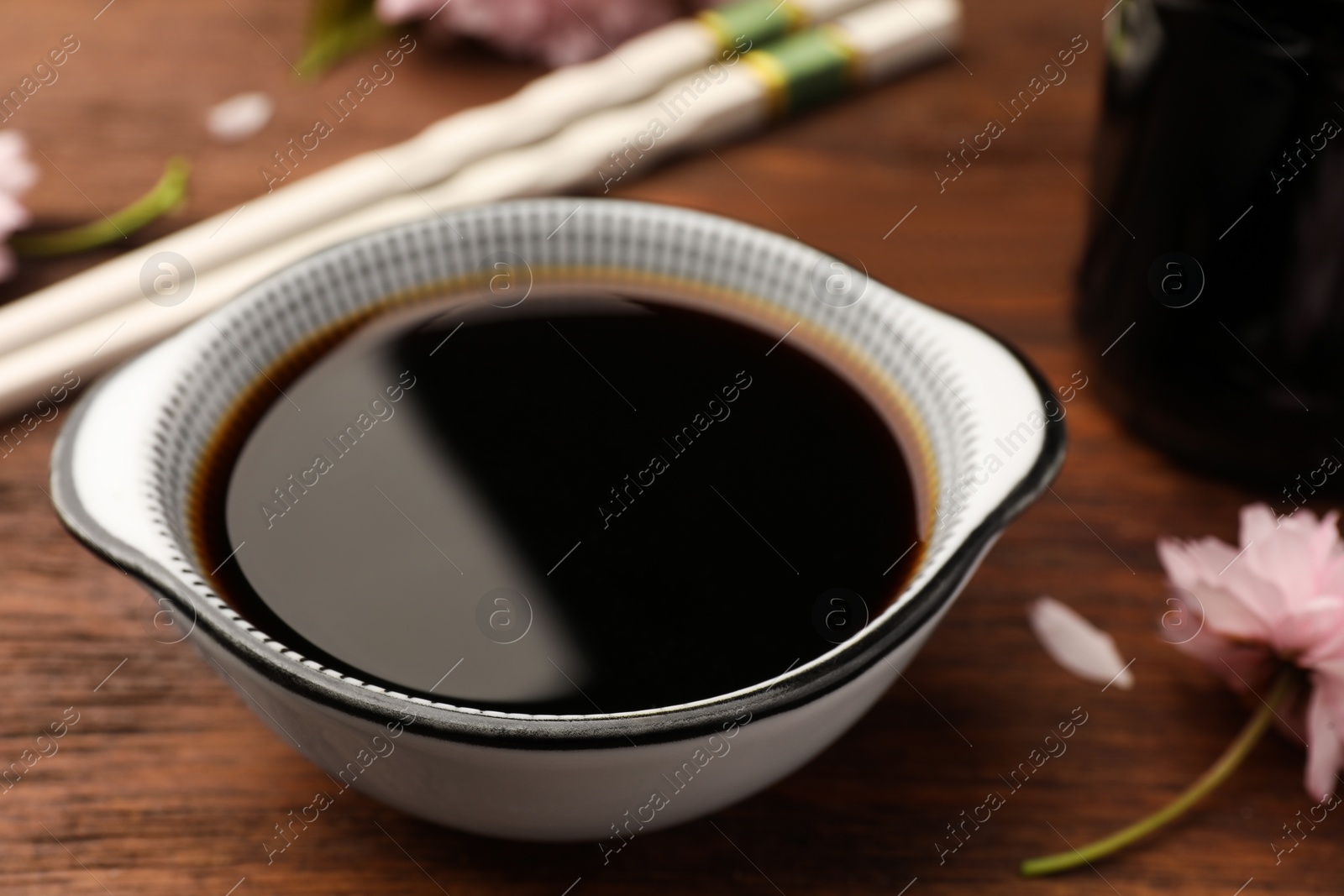 Photo of Bowl with soy sauce on wooden table, closeup