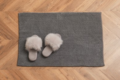 Photo of New grey bath mat with fluffy slippers on floor, top view